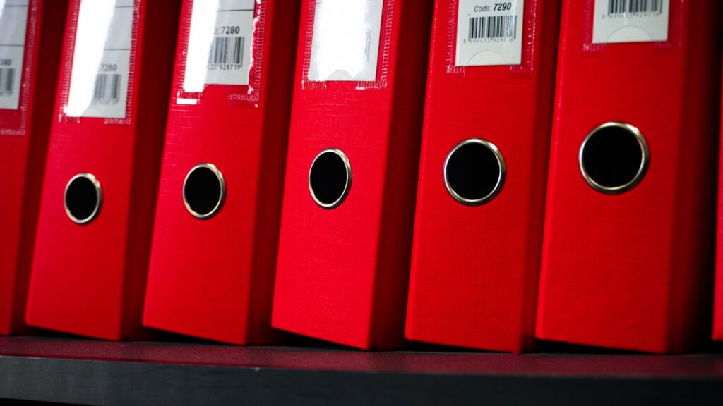 Rote Aktenordner stehen aufgereiht in einem Regal